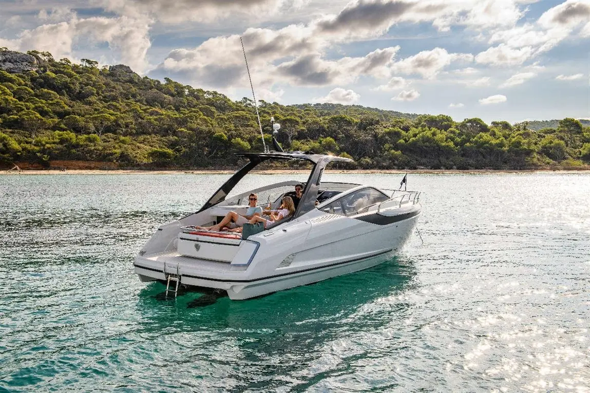 A sleek white motorboat cruises in clear waters, with three people relaxing aboard against a backdrop of green hills.